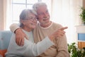 Smiling senior couple sitting at home hugging. Woman wearing eyeglasses indicating with a finger.  bright light from window Royalty Free Stock Photo