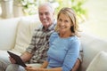 Smiling senior couple sitting on sofa with digital tablet in living room Royalty Free Stock Photo