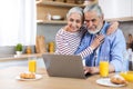 Smiling senior couple using laptop in kitchen while having breakfast together Royalty Free Stock Photo