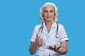 Smiling senior doctor using transparent digital tablet and showing thumb up gesture on blue background. Royalty Free Stock Photo