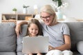 Smiling grandma and cute kid granddaughter watching cartoons on