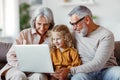 Smiling senior grandparents and cute little girl granddaughter watching cartoons on laptop Royalty Free Stock Photo