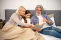 Smiling senior grandparents reading book with little girl lying on bed Royalty Free Stock Photo