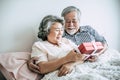 Smiling senior husband making giving gift box to his wife in bedroom