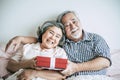 Smiling senior husband making giving gift box to his wife in bedroom