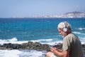 Smiling senior man, beard and white hair, using phone at sea in windy day. Elderly people enjoying holiday and beauty in nature Royalty Free Stock Photo