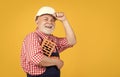 smiling senior man bricklayer in hard hat on yellow background