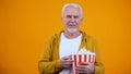 Smiling senior man with pop corn watching exciting film, spending leisure time