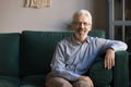 Smiling senior man sit on sofa in living room, portrait