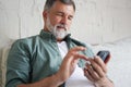 Smiling Senior Man Using Cellphone Browsing Internet Sitting On Sofa Indoor. Royalty Free Stock Photo