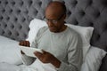 Smiling senior man using digital tablet while resting on bed Royalty Free Stock Photo