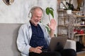 Smiling senior man wear earphones wave to camera having video call on laptop. Royalty Free Stock Photo