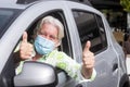 Smiling Senior Man Wearing Surgical Mask Due To Covid19 Coronavirus Parked With His Silver Car Gesturing Ok Sign With Both Hands