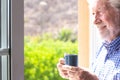 Smiling senior man at the window holding a coffee cup looking out Royalty Free Stock Photo