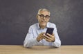 Smiling senior man writes message or browses news on Internet using modern mobile phone. Royalty Free Stock Photo