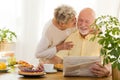 Smiling senior man reading newspaper and his wife kissing him