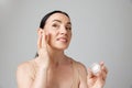 Smiling senior woman applying anti-aging cream to hide wrinkles below eyes. Beauty skin care in old age. Royalty Free Stock Photo