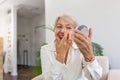 Smiling senior woman applying anti-aging lotion to remove dark circles under eyes. Happy mature woman using cosmetic cream to hide Royalty Free Stock Photo