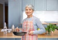 smiling senior woman in apron with frying pan