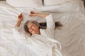 Smiling senior woman in a bathrobe lying on a bed and looking away. Female relaxing in a hotel room