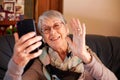 Smiling Senior Woman At Home Waving As She Makes Video Call To Family On Mobile Phone Royalty Free Stock Photo