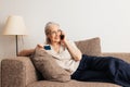 Smiling senior woman making a call via mobile phone and holding a credit card while lying on sofa Royalty Free Stock Photo
