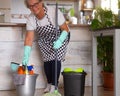 Smiling senior woman ready to start with the housework. Close to she a plastic bucket with items for cleaning. One alone people