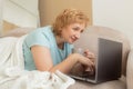 Smiling senior woman relaxing in home bedroom using laptop watching video or movie enjoying technology, leisure time, retirement