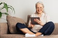 Smiling senior woman sitting with crossed legs using a digital tablet. Aged female in eyeglasses reading from a digital tablet at Royalty Free Stock Photo