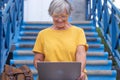 Smiling senior woman sitting outdoors on staircases  using laptop computer. Active blogger worker nomadic people Royalty Free Stock Photo