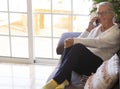 Smiling senior woman sitting on the sofa at home talking with friends at her smart phone - attractive woman with white hair and Royalty Free Stock Photo