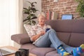 Smiling senior woman sitting on sofa at home using mobile phone and laptop Royalty Free Stock Photo