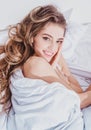 Smiling sensual woman laying in bed under a duvet in bedroom. Good morning. Royalty Free Stock Photo