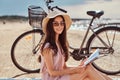 Smiling sensual young woman holds a book and looking at camera while sitting on the beach, enjoying the vacation. Royalty Free Stock Photo