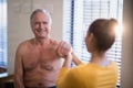 Smiling shirtless senior male patient looking at female therapist giving arm massage Royalty Free Stock Photo
