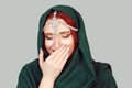 Smiling shy. Beautiful Muslim woman with green scarf hijab and oriental jewelry on head smile hand on face isolated white light Royalty Free Stock Photo