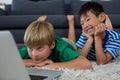 Smiling siblings lying on rug and using laptop in living room