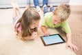 Smiling siblings lying on the rug using a tablet