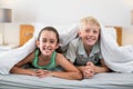 Smiling siblings lying under bed sheet in bedroom Royalty Free Stock Photo