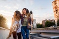 Smiling skate girls holding long-boards walking outdoors in the street