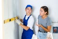 Young contractor with female homeowner checking wall flatness with level meter Royalty Free Stock Photo