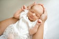 Smiling sleeping cute little baby girl under 1 year old wear white dress lying on mother hands in room at home close up. Top view Royalty Free Stock Photo