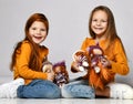 Smiling small girls sisters or friends in yellow longsleeves, jeans and sneakers sitting on floor and playing with toy