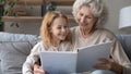 Smiling small granddaughter and mature grandma enjoy interesting book together Royalty Free Stock Photo