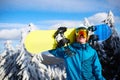 Smiling snowboarder posing carrying snowboard on shoulder at ski resort near forest before backcountry freeride and