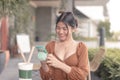 A smiling Southeast Asian woman is using her mobile phone while sitting outside the cafe as she messages her boyfriend