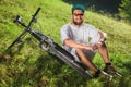 Smiling sport boy sit on the grass near the bicycle outdoor