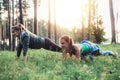 Smiling sportswomen having outdoor morning training standing in plank pose on grass in park