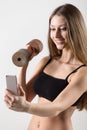 Smiling sporty girl holding dumbbell and taking selfie with smartphone Royalty Free Stock Photo