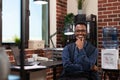 Smiling startup employee with glasses posing casual with hand up to chin sitting at desk